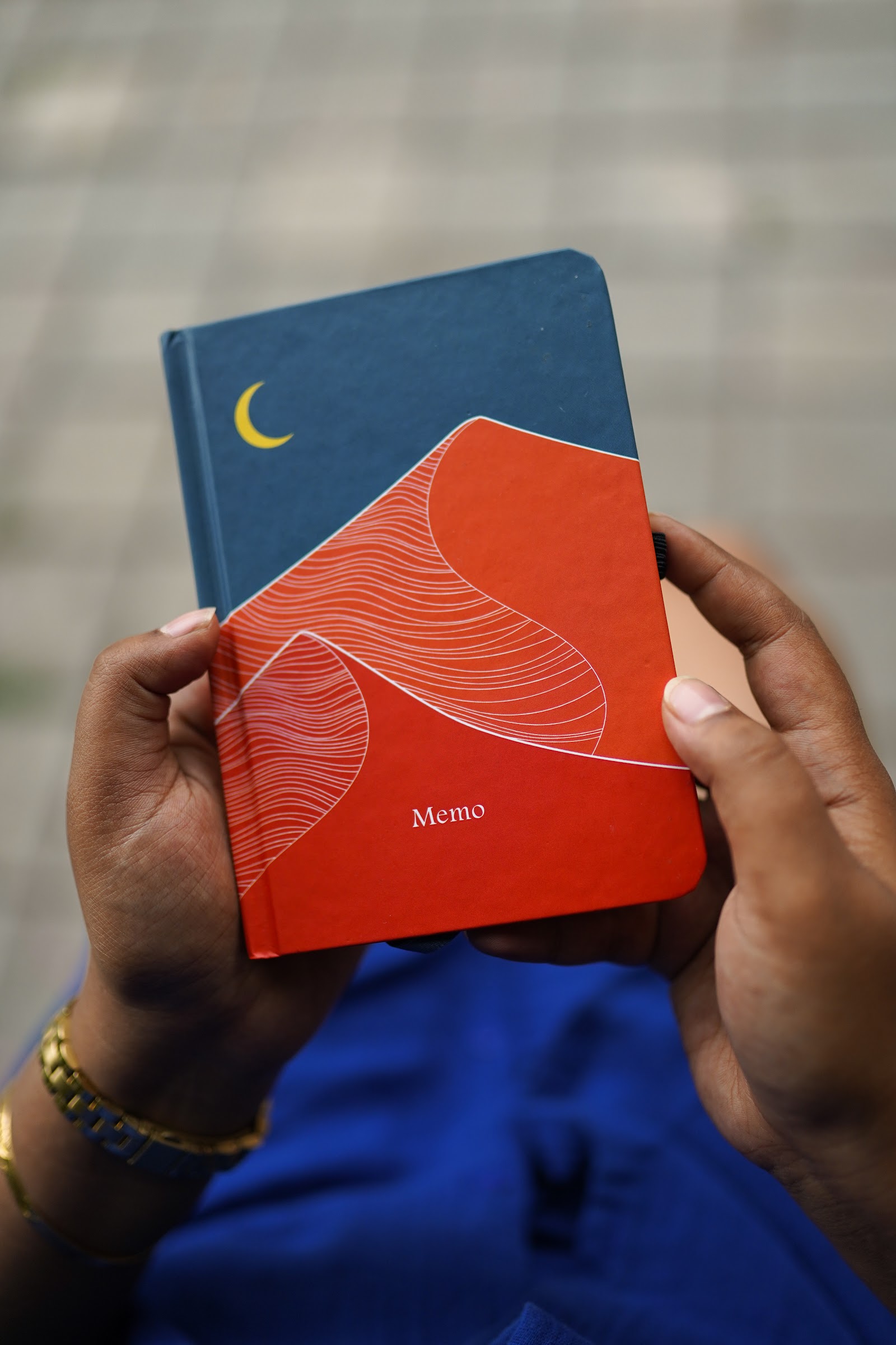Hands holding a hardbound notebook printed with orange dunes under a yellow crescent moon