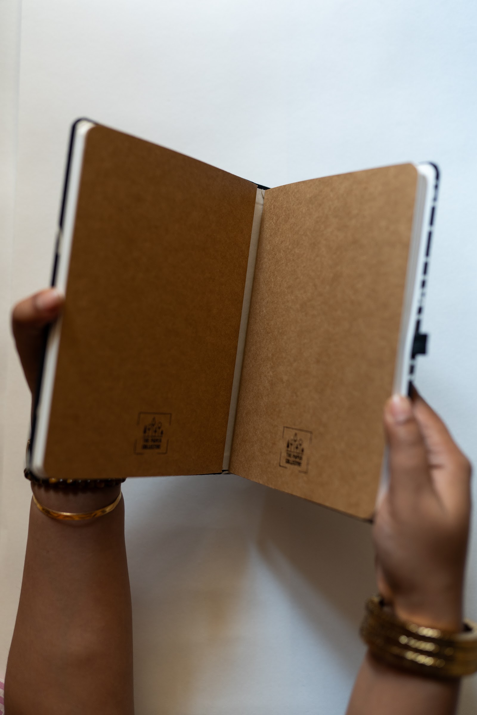 Two hands opening a notebook flat to show kraft endpapers blind-stamped with the workshop mark