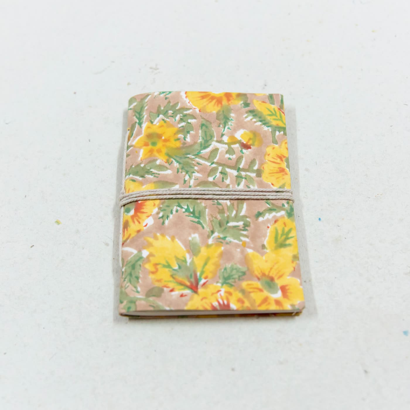 A pocket notebook in cotton printed with yellow flowers and green leaves, closed with a cord